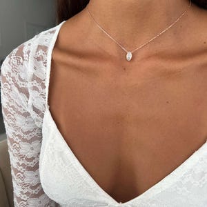 May include: A delicate rose gold necklace with a small, oval-shaped pendant. The pendant is centered on the neckline. The necklace is worn with a white lace top.