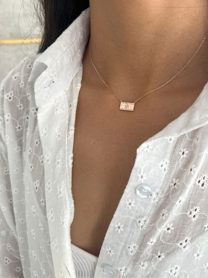 May include: A delicate gold chain necklace with a small rectangular pendant featuring a star design. The pendant is set with tiny sparkling stones.