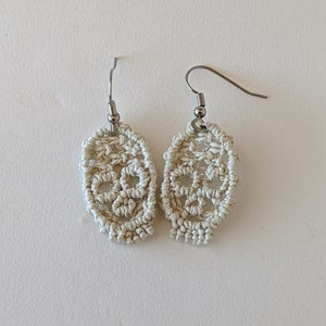 May include: A pair of white crocheted skull earrings with silver hooks.