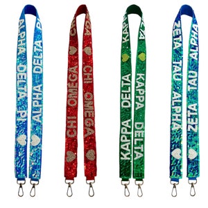 May include: Four different sorority lanyard straps with the sorority names and symbols. The straps are blue, red, green, and teal with white lettering and gold hearts.