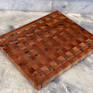 May include: A large, rectangular wooden cutting board with a checkered pattern. The board is made of different shades of brown wood and has a light brown border.