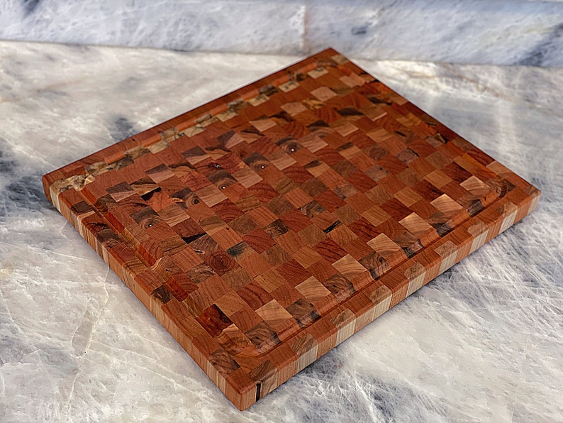 May include: A large, rectangular wooden cutting board with a checkered pattern. The board is made of different shades of brown wood and has a light brown border.