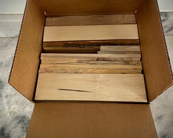 May include: A cardboard box is open and filled with various pieces of wood. The wood is stacked neatly and appears to be different types of wood, including maple and walnut.