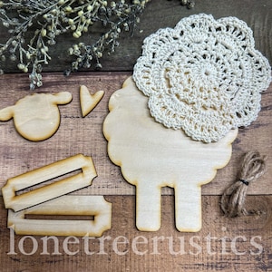 May include: Wooden sheep-shaped craft pieces with a cream-colored crocheted doily, a small wooden arrow, and two wooden rectangular pieces. A bundle of twine is also included. The text "lonetree rustics" is visible.