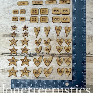 May include: A collection of wooden buttons in various shapes, including rectangles, squares, stars, and hearts. The buttons are light brown and have two or four holes for sewing. A ruler is placed next to the buttons. The text "lonetreerustics" is at the bottom.