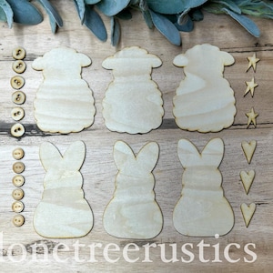 May include: Wooden sheep and bunny cutouts, stars, hearts, and buttons arranged on a wooden surface. The sheep and bunny shapes are light-colored, with visible wood grain. The buttons are small and round. The text "lonetreerustics" is at the bottom.