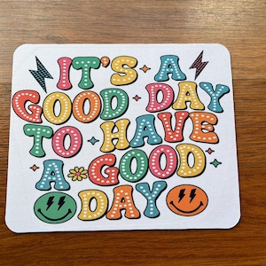 May include: White mouse pad with a colorful retro design that says "It's a good day to have a good day".