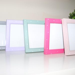 May include: Five picture frames in different colours, including grey, lavender, mint green, pink, and light pink. Each frame has a white polka dot pattern.