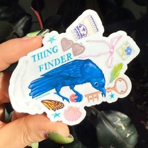 May include: A white sticker featuring a blue bird, a key, a seashell, a butterfly, and the text "THING FINDER".