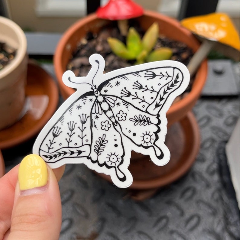 Peut inclure: Un autocollant noir et blanc d'un papillon avec des motifs floraux complexes. Le papillon a un motif d&eacute;taill&eacute; de fleurs, de feuilles et de volutes.