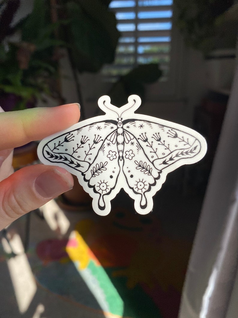 Peut inclure: Un autocollant blanc avec un dessin au trait noir d'un papillon avec des d&eacute;tails floraux. Le papillon a un corps stylis&eacute; avec de grandes ailes et un motif d&eacute;licat de fleurs et de feuilles.