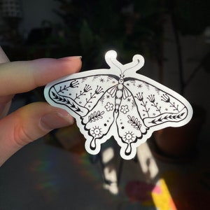 Peut inclure: Un autocollant noir et blanc repr&eacute;sentant un papillon avec des d&eacute;tails floraux. Le papillon a un design stylis&eacute; avec des motifs complexes et une ambiance fantaisiste.