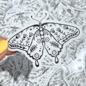 Peut inclure: Autocollant noir et blanc d'un papillon avec des motifs floraux complexes. Le papillon a une forme de c&oelig;ur au centre de son corps.