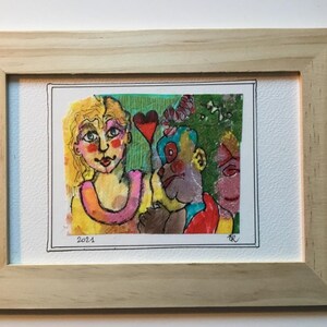 Könnte beinhalten: Ein gerahmtes Mixed-Media-Kunstwerk mit drei Gesichtern, zwei weiblichen und einem männlichen, mit einem roten Herzen und grünem Hintergrund. Das Kunstwerk ist mit "KR" signiert und mit "2021" datiert.