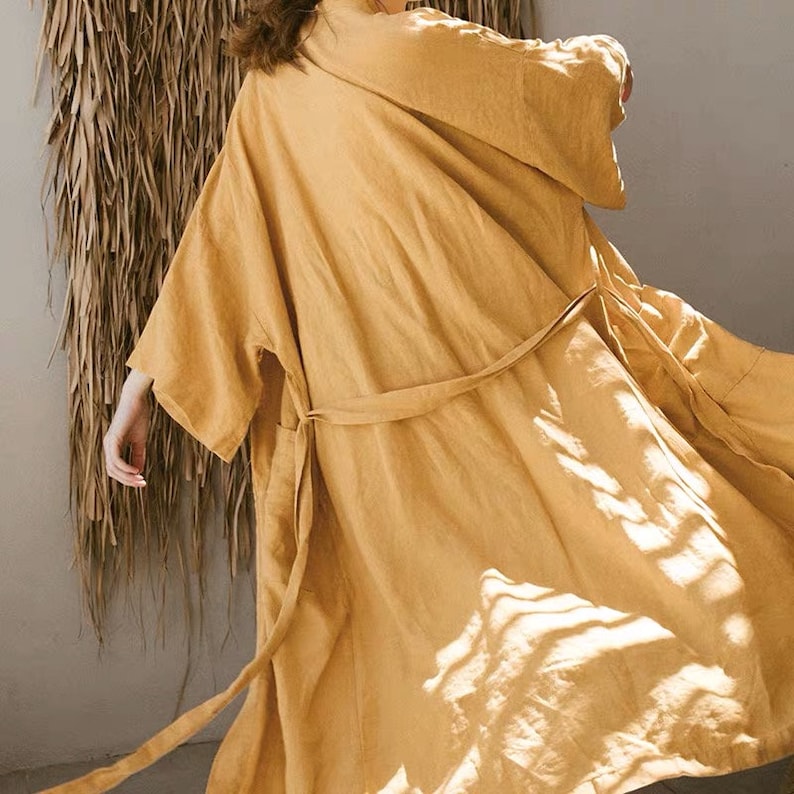 May include: A long, flowing, mustard yellow linen robe with a self-tie belt. The robe is made of a lightweight, breathable fabric and has a relaxed fit.