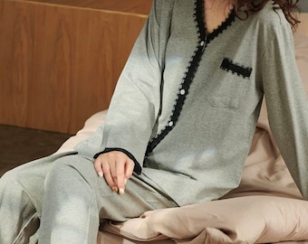 Puede incluir: Una camiseta de pijama gris de manga larga con ribete de encaje negro y cierre de botones. La camiseta tiene cuello en V y un bolsillo en el lado izquierdo.