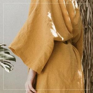 May include: A mustard yellow linen robe with long sleeves and a sash tie. The robe is made of a soft, lightweight fabric and has a relaxed fit.