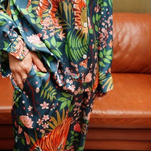 Puede incluir: Conjunto de pijama de color turquesa con un estampado floral y de tigre vibrante. La parte superior de manga larga tiene botones blancos y un bolsillo. El pantal&oacute;n a juego es visible. La tela tiene un brillo sedoso.
