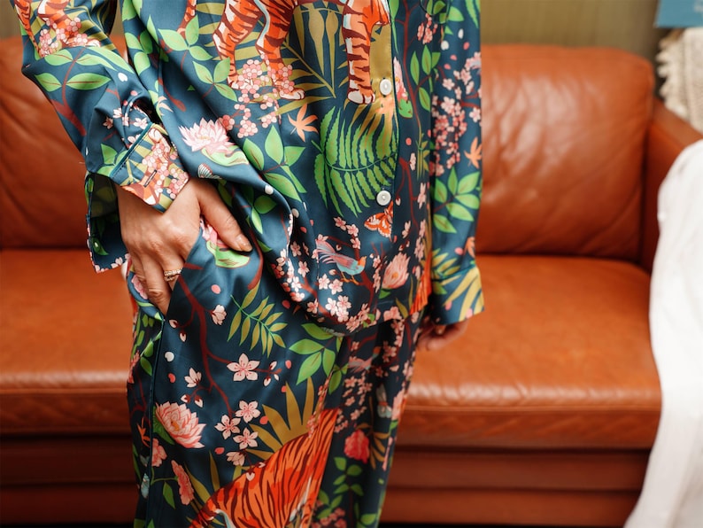 Puede incluir: Conjunto de pijama de color turquesa con un estampado floral y de tigre vibrante. La parte superior de manga larga tiene botones blancos y un bolsillo. El pantal&oacute;n a juego es visible. La tela tiene un brillo sedoso.