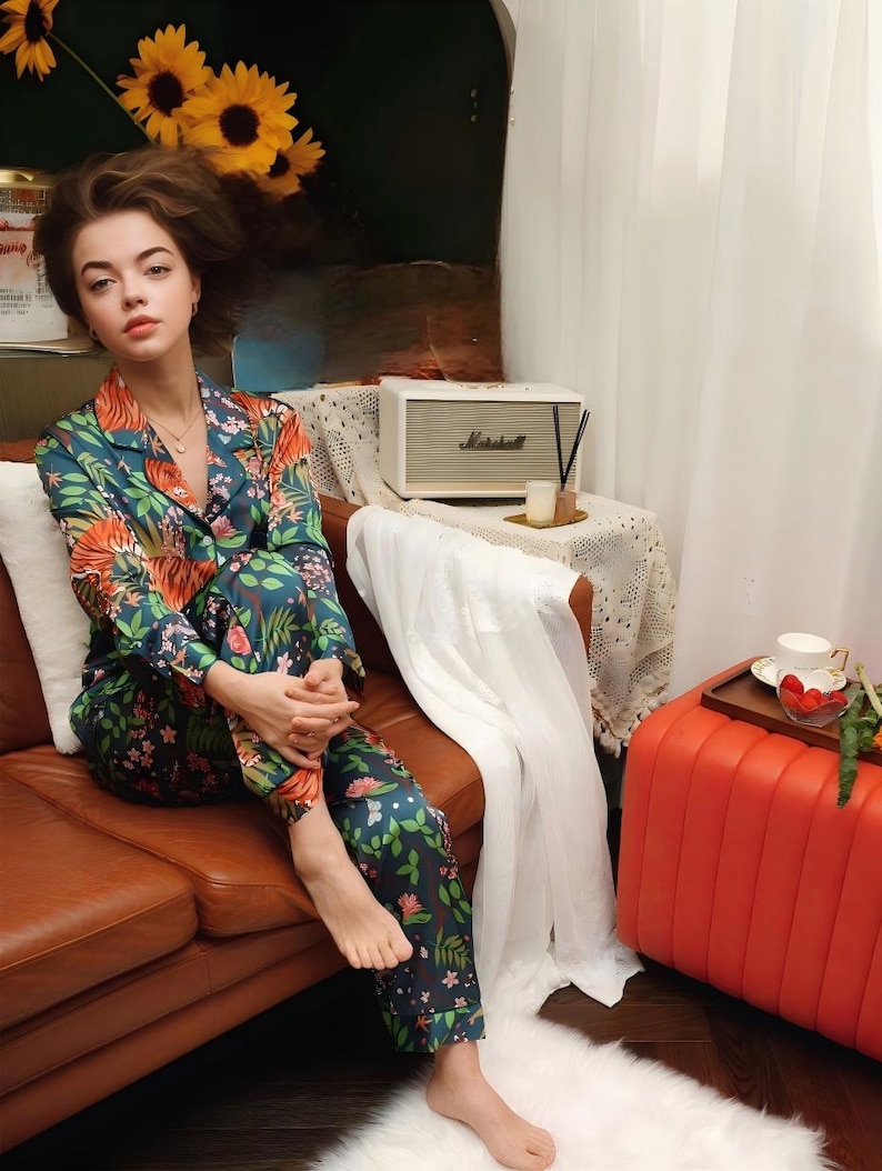 Puede incluir: Una persona con un conjunto de pijama con estampado floral en tonos verde azulado, naranja y rosa. El conjunto incluye una camisa con botones y pantalones a juego. La persona est&aacute; sentada en un sof&aacute; de cuero marr&oacute;n.