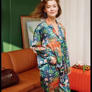 Puede incluir: Un conjunto de pijama de color verde azulado con un estampado floral y de tigre vibrante. La parte superior de manga larga tiene cuello y cierre de botones. Los pantalones a juego completan el conjunto. Los pijamas son de material sedoso.