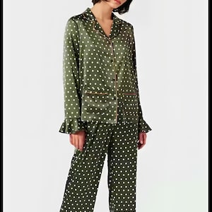 Könnte beinhalten: Olivgrünes Pyjama-Set mit weißen Polka-Dots. Das langärmlige Oberteil hat einen Reverskragen, eine Knopfleiste und Rüschenbündchen. Die passende Hose ist weit geschnitten. Das Set ist mit einer dünnen, hellbraunen Paspel versehen.