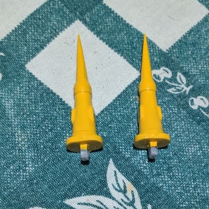 Pode incluir: Dois objetos pontiagudos de metal amarelo com uma base arredondada. Os objetos estão sobre um tecido estampado verde e branco.