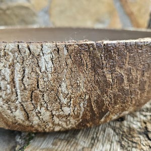 Peut inclure: Gros plan sur un bol rond artisanal avec un extérieur texturé en forme d'écorce. La surface du bol est un mélange de tons bruns et beiges, avec des fissures et des imperfections visibles, lui donnant un aspect rustique. Le bol est probablement en bois ou dans un matériau similaire.