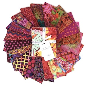 May include: A collection of 18 fabric squares in various shades of red, orange, and pink with floral, geometric, and abstract patterns. The fabric squares are arranged in a circle with a larger square in the center. The larger square has a white background with a floral pattern and the text "Free Spirit" printed on it.