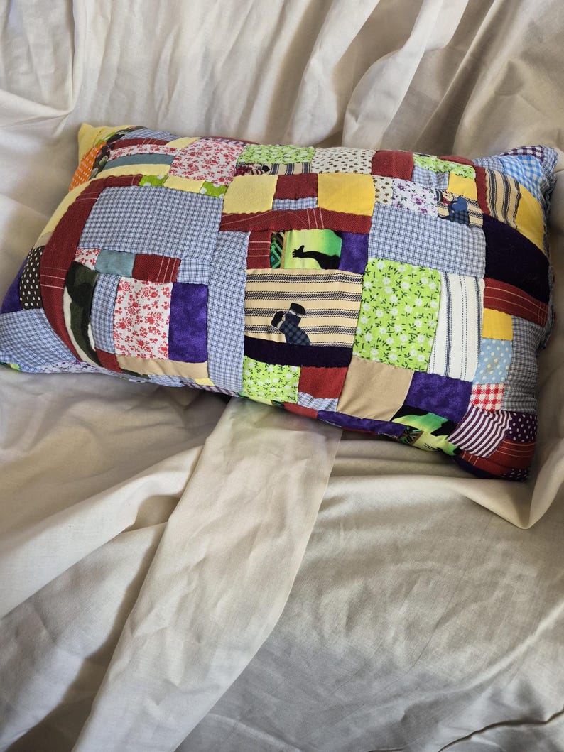 以下が含まれることがあります： 花柄、ギンガムチェック、ストライプなど、さまざまな生地の模様と色を使用した長方形のパッチワーク枕。枕は柔らかく、質感のある外観で、ふわふわの素材が詰められています。枕は白いシーツの上に置かれています。