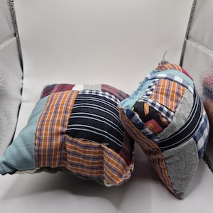 May include: Two small, handmade patchwork pillows. The pillows are made from various fabric scraps in a mix of colors and patterns, including stripes, checks, and solid colors. The fabrics include blue, orange, red, and gray.