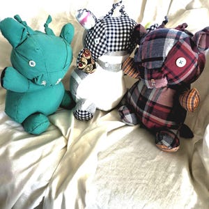 May include: Three stuffed animal toys made from fabric. The left toy is solid teal with a white button eye. The center toy features a black and white gingham pattern with a white button eye. The right toy is made of red, black, and grey plaid fabric.