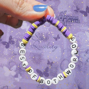 May include: A beaded bracelet with the words "BEST OF BOTH WORLDS" in white letter beads. The bracelet features purple and yellow disc beads. The background is a purple surface with butterfly and floral patterns.