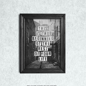 May include: Black and white photograph print in a black frame with the text "This is the beginning of the rest of your life" printed on it. The photo shows a narrow alleyway in a city.