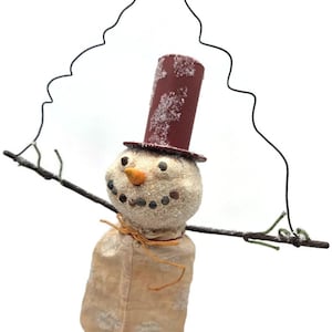 May include: A handcrafted snowman ornament with a burgundy top hat and twig arms. The snowman's face has a carrot nose and stone eyes. The body is a beige sack, and the ornament hangs from a wire. A charming winter decoration.