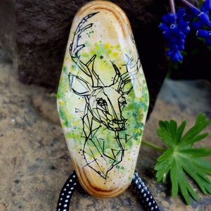 May include: A wooden pendant featuring a geometric deer design painted in black ink on a green and yellow background. The pendant is attached to a black cord with white polka dots.