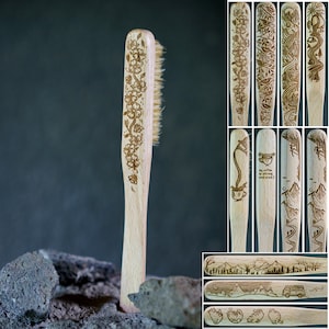 Può includere: Uno spazzolino di legno con un design floreale e setole naturali. Lo spazzolino è mostrato su uno sfondo scuro con alcune rocce.