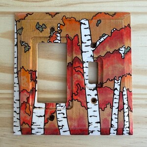 May include: Hand-painted wooden light switch cover featuring a birch tree design. The cover has a rectangular shape with cutouts for the switch and screws. The artwork includes white birch trunks, red and orange foliage, and black outlines.