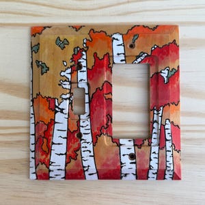 May include: Hand-painted light switch cover featuring a birch tree forest design. The cover has a square shape with a rectangular opening. The artwork includes white birch tree trunks, red and orange leaves, and a light brown background.