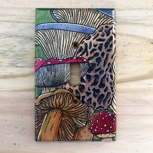May include: A light switch cover with a colorful mushroom design. The cover features a variety of mushrooms with red, brown, and yellow caps, and green and brown stems. The mushrooms are drawn in a detailed, realistic style.