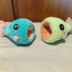 May include: Two handmade crochet fish toys. One is turquoise with a pink fin and a pink mouth, the other is light green with a peach mouth and a gray fin. Both have black button eyes.