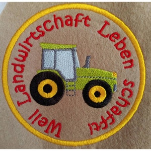 Könnte beinhalten: Ein runder, gelb umrandeter Aufnäher mit rotem Text, der "Landwirtschaft Leben schaffen" lautet, und einem grünen Traktor mit schwarzen Rädern und gelben Zentren.