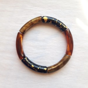 Armband gemaakt van gebogen acrylbuisjes met kralen in goudbruin/topaas/goudzwart.