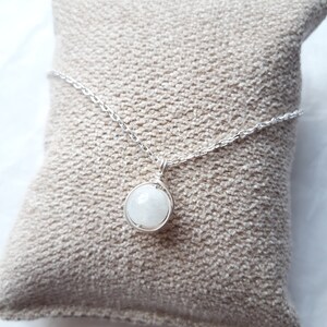 May include: A silver chain necklace with a white gemstone pendant. The pendant is wrapped in silver wire and the gemstone is round.