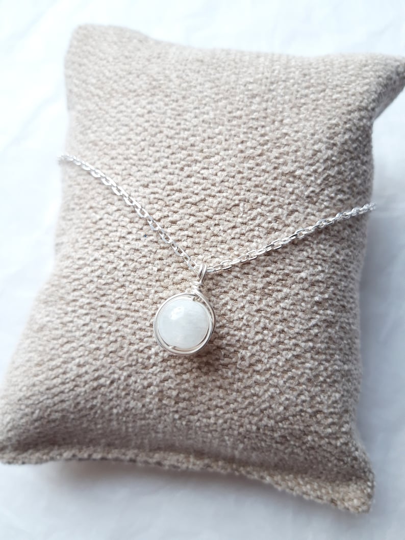 May include: A silver chain necklace with a white gemstone pendant. The pendant is wrapped in silver wire and the gemstone is round.