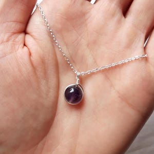 May include: A silver chain necklace with a small, round, purple amethyst gemstone pendant.