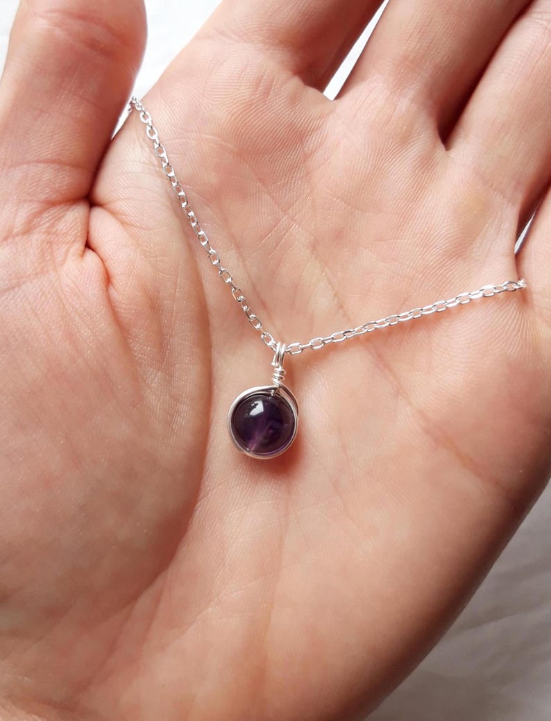 May include: A silver chain necklace with a small, round, purple amethyst gemstone pendant.