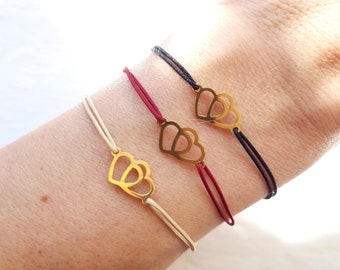 May include: Three adjustable bracelets with a gold double heart charm. The bracelets are available in black, red, and cream.
