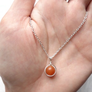 May include: A silver chain necklace with a small, round, orange gemstone pendant.