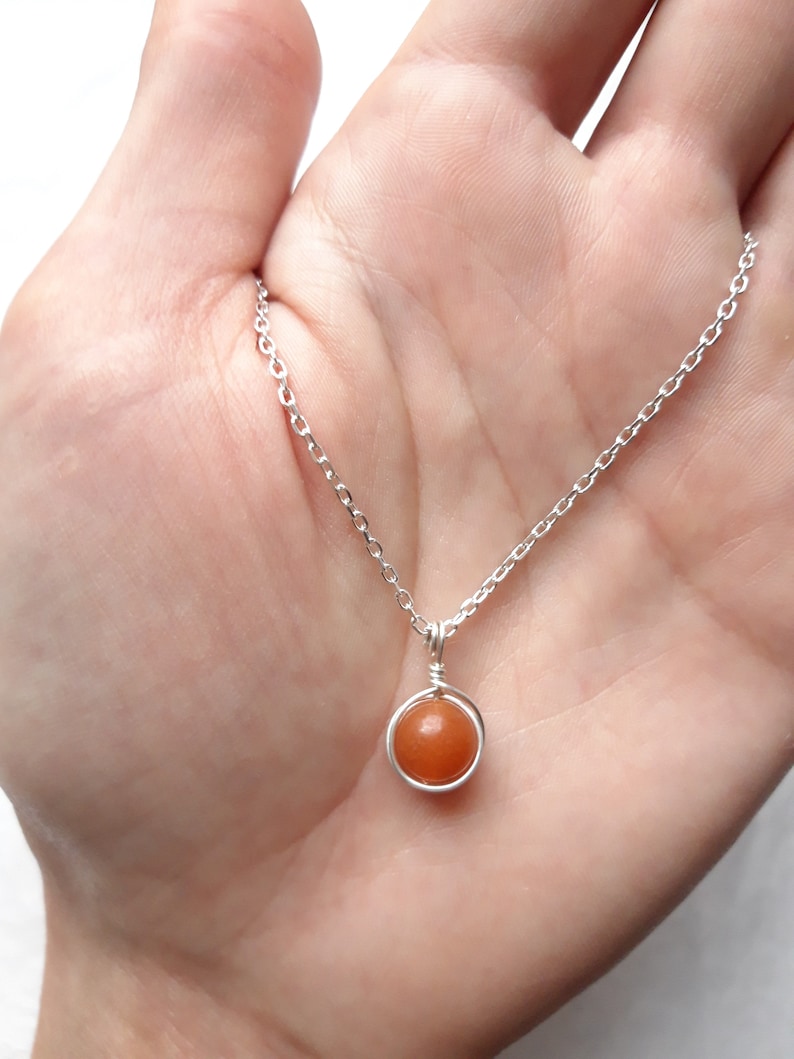 May include: A silver chain necklace with a small, round, orange gemstone pendant.